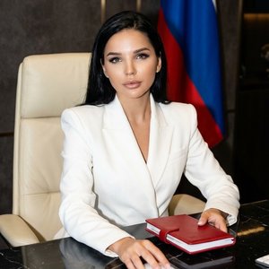 5.Мощная и элегантная молодая женщина сидит уверенно за гладким черным мраморным столом в роскошном офисе топ-менеджера. На ней — объемный белый пиджак с четкими линиями и широкими плечами, волосы уложены аккуратно. Макияж безупречный: мягкий смоки-айс, г
