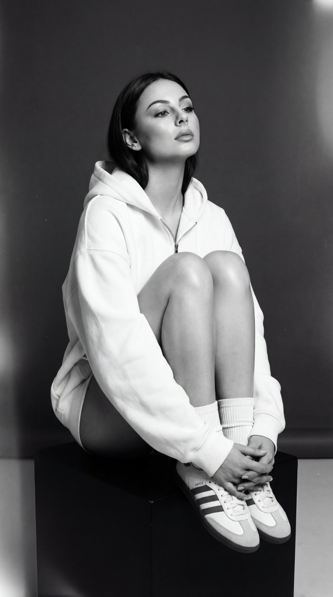 A girl — vertical professional portrait, full seated crop from top of head to shoes, camera positioned at slight low‑to‑eye level (mild upward tilt), shallow depth of field for subject separation.

Pose and hands:
⦁ Sitting on a low black cube, torso lean