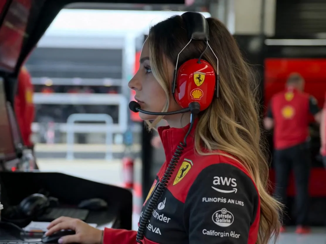 Ultra realistic cinematic
Formula 1 paddock video of the woman from the reference image inside the Ferrari F1 garage during a live qualifying session. She is wearing a red Ferrari team headset with microphone while watching the race intensely. Realistic S