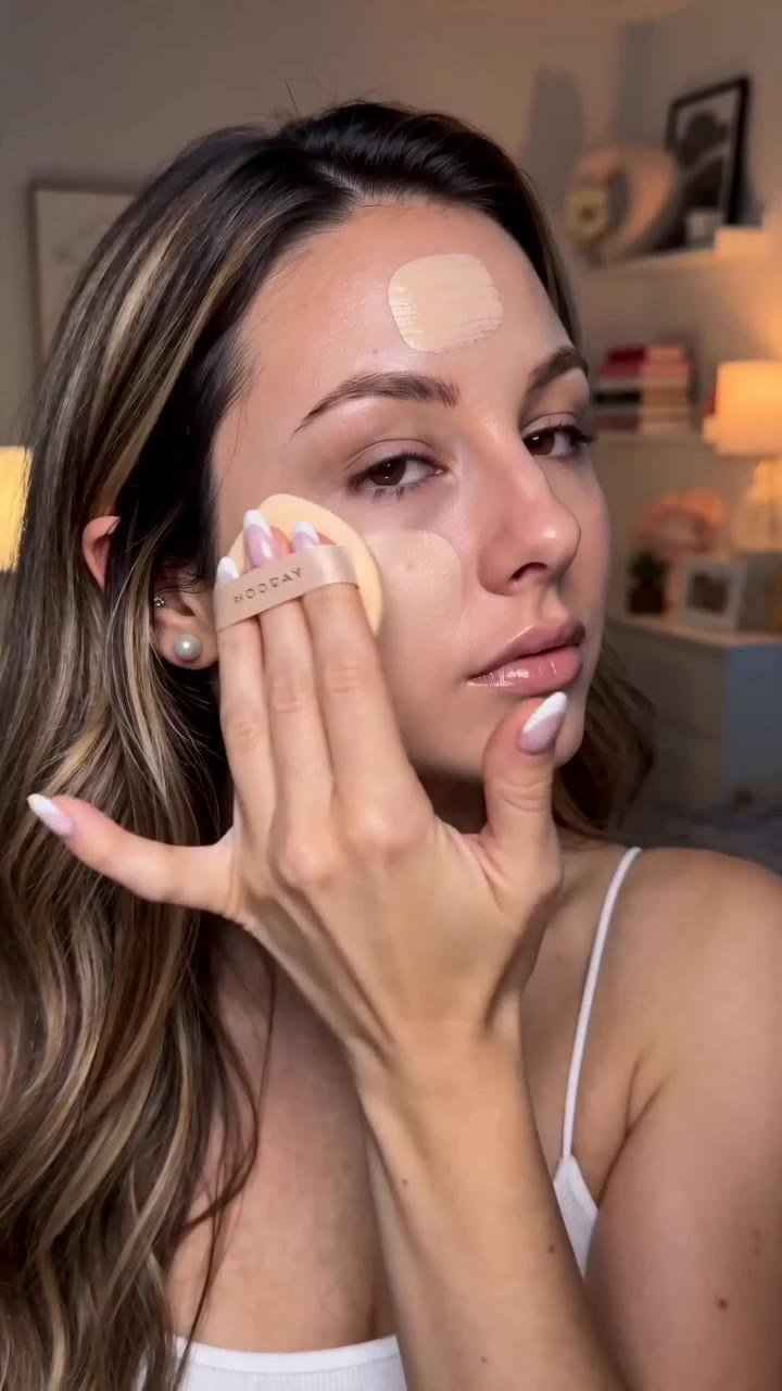 A high-quality, realistic ASMR-style beauty vlog. Split-screen transition or a fast-paced montage of a charismatic female beauty influencer doing her evening makeup. 
1. Close-up of her applying liquid foundation with a damp beauty blender, realistic skin