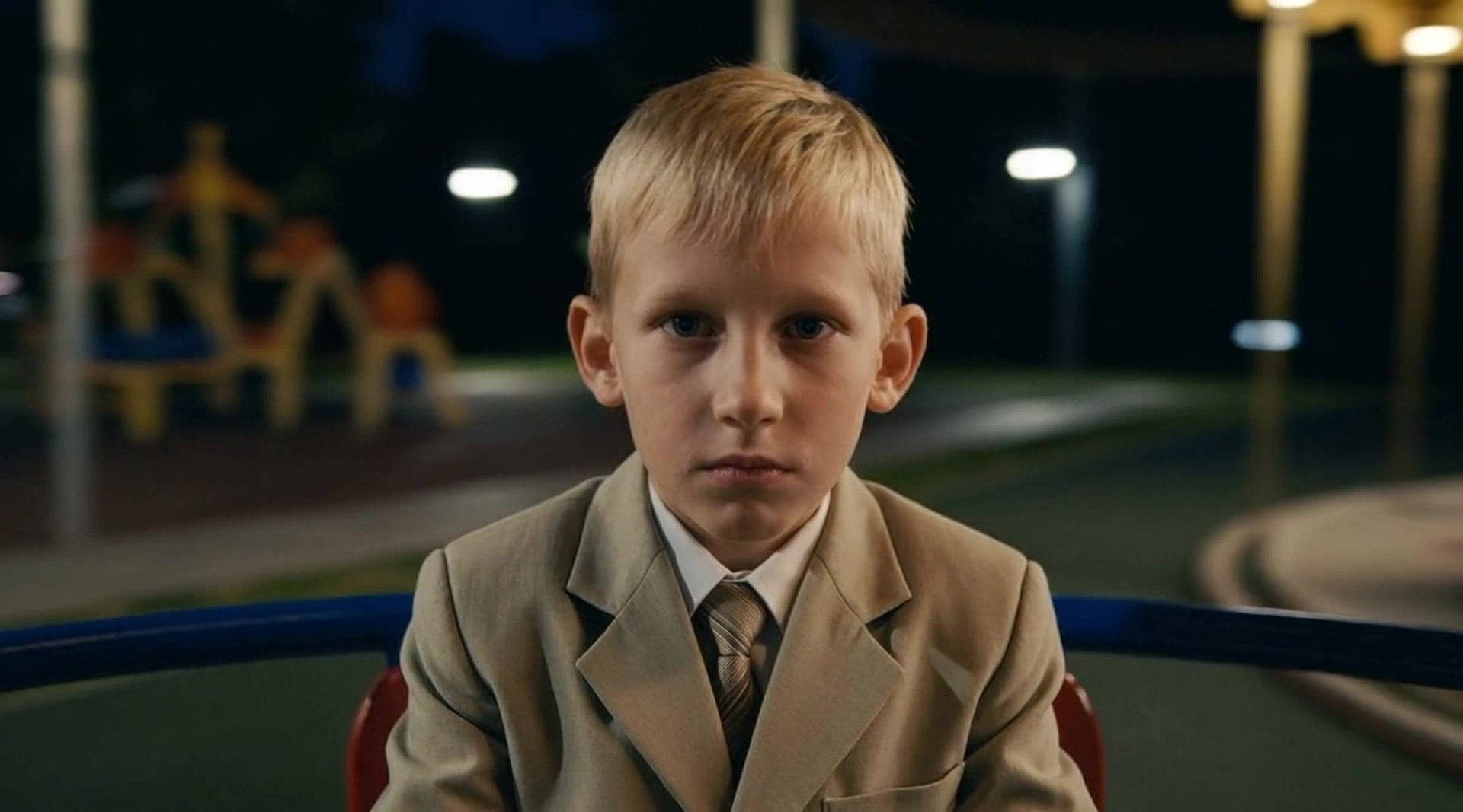 The character should appear seated on a carousel at a children's playground, with only the face and part of the torso visible in the frame. The background softly rotates in a circular motion, creating a sense of movement and speed. The facial expression i