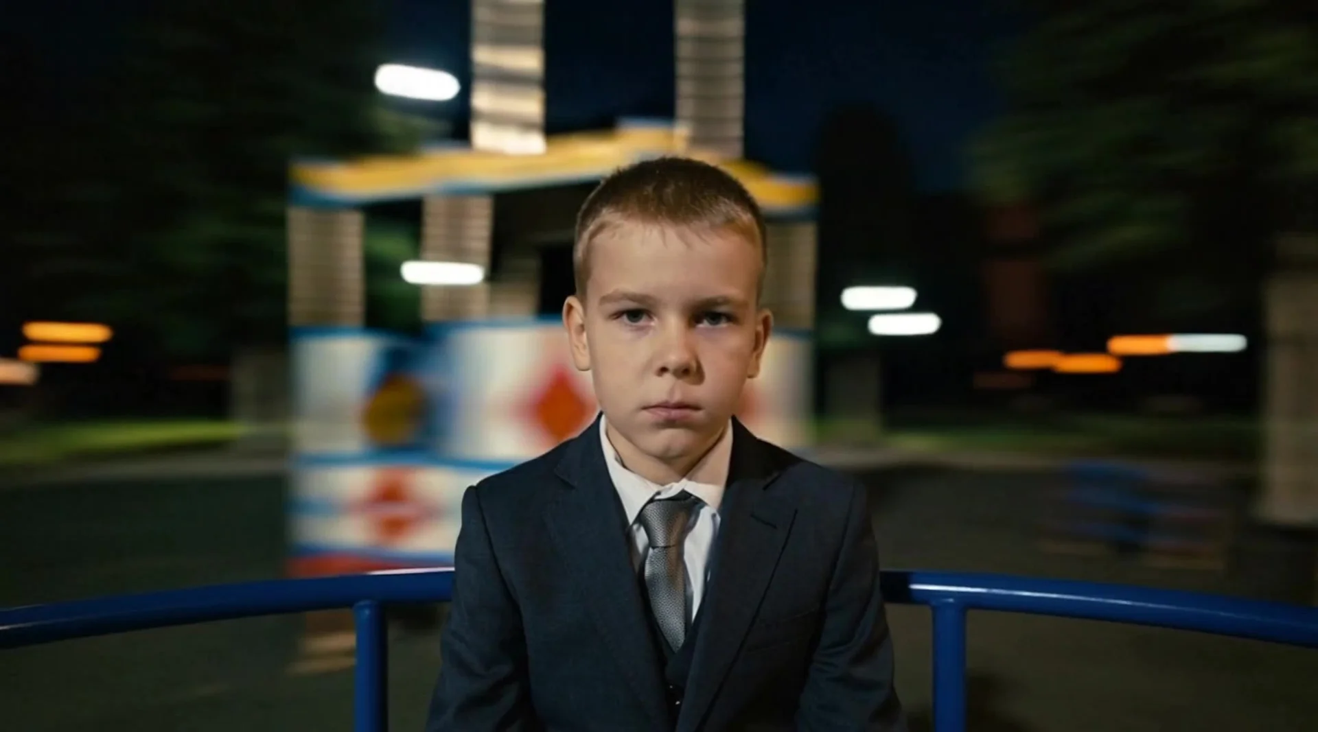 The character should appear seated on a carousel at a children's playground, with only the face and part of the torso visible in the frame. The background softly rotates in a circular motion, creating a sense of movement and speed. The facial expression i