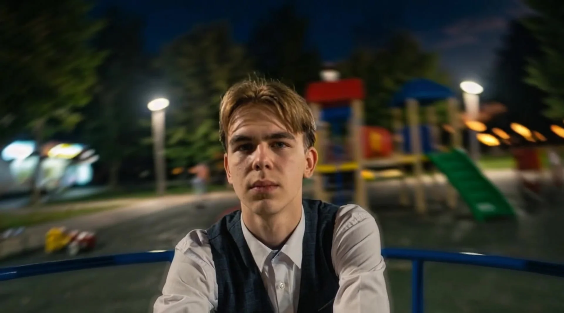 The character should appear seated on a carousel at a children's playground, with only the face and part of the torso visible in the frame. The background softly rotates in a circular motion, creating a sense of movement and speed. The facial expression i